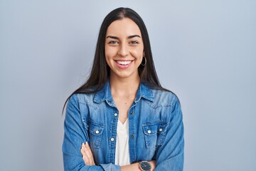 Hispanic woman standing over blue background happy face smiling with crossed arms looking at the camera. positive person.