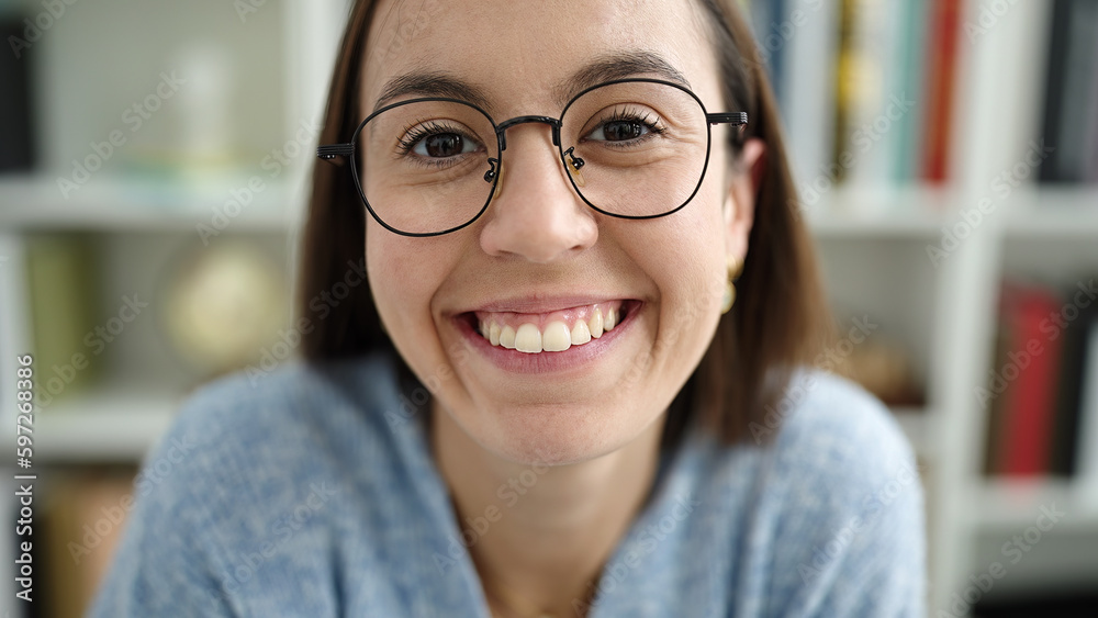 Wall mural Young beautiful hispanic woman student smiling confident sitting on table at library university