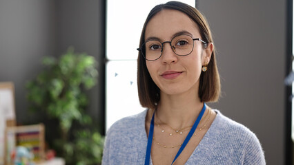 Young beautiful hispanic woman teacher standing with relaxed expression at kindergarten