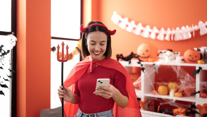 Young beautiful hispanic woman wearing devil costume using smartphone at home