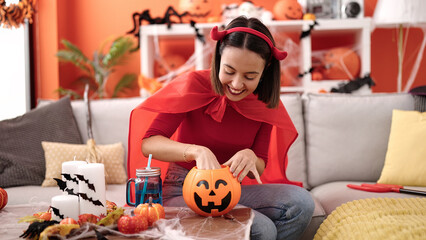 Young beautiful hispanic woman wearing devil costume holing sweet of pumpkin basket at home