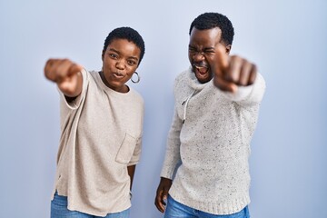 Young african american couple standing over blue background together pointing displeased and frustrated to the camera, angry and furious with you