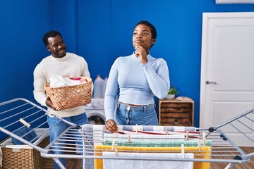 Young african american couple hanging clothes at clothesline serious face thinking about question with hand on chin, thoughtful about confusing idea