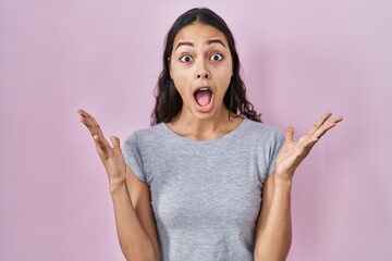 Young brazilian woman wearing casual t shirt over pink background celebrating crazy and amazed for...