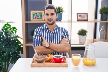 Fototapeta na wymiar Hispanic man with long hair sitting on the table having breakfast skeptic and nervous, disapproving expression on face with crossed arms. negative person.