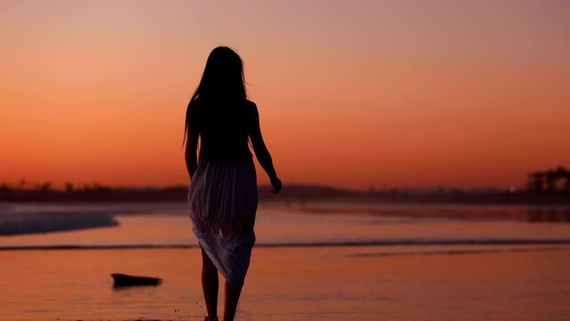 Pretty Asian woman enjoys a walk on the beach at sunset. Slow Motion.