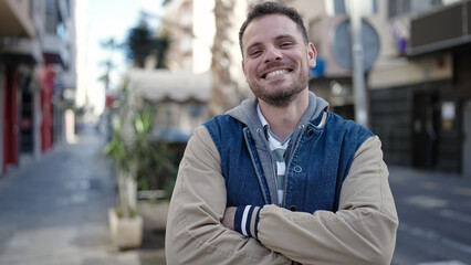 Young caucasian man smiling with crossed arms at street