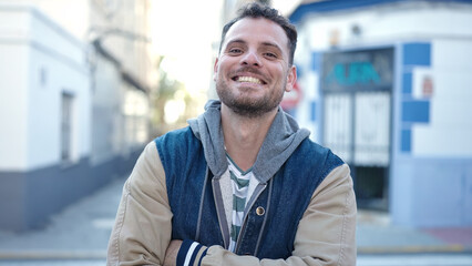Young caucasian man smiling with crossed arms at street