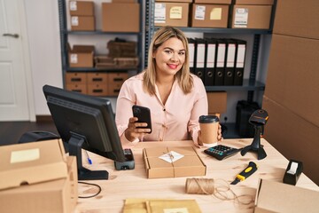 Young hispanic woman ecommerce business worker using smartphone and drinking coffee at office