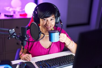 Middle age chinese woman streamer playing video game drinking coffee at gaming room