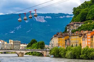 Isere river in Grenoble city skyline, Auvergne-Rhone-Alpes region, France. Pont Marius-Gontard bridge, Grenoble-Bastille Cable car (Telepherique) and Alps mountains on background - obrazy, fototapety, plakaty