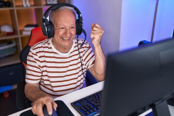 Middle age grey-haired man streamer playing video game with winner expression at gaming room