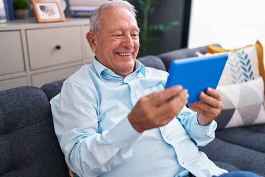 Middle age grey-haired man using touchpad sitting on sofa at home