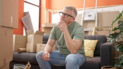 Middle age grey-haired man sitting on sofa with stressed expression at new home