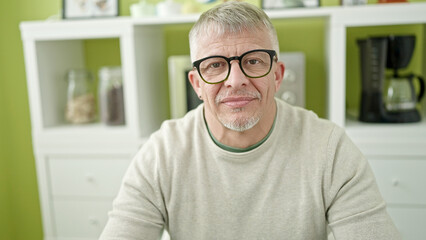 Middle age grey-haired man sitting on table with relaxed expression at home