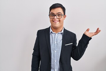 Young hispanic man with down syndrome wearing business style smiling cheerful presenting and pointing with palm of hand looking at the camera.