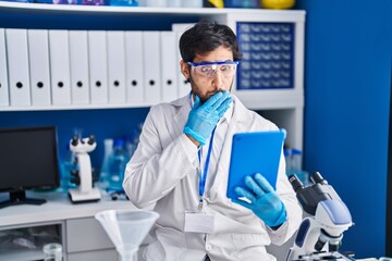 Handsome latin man working at scientist laboratory using tablet covering mouth with hand, shocked and afraid for mistake. surprised expression