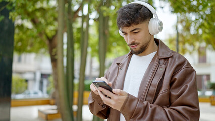 Young arab man listening to music with relaxed expression at park