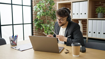 Fototapeta premium Young arab man business worker listening to music doing drummer gesture at office