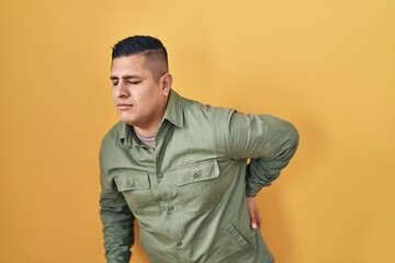 Hispanic young man standing over yellow background suffering of backache, touching back with hand, muscular pain