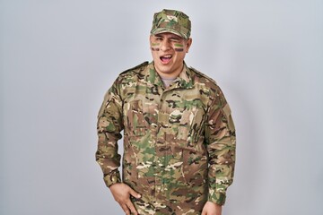 Hispanic young man wearing camouflage army uniform winking looking at the camera with sexy...