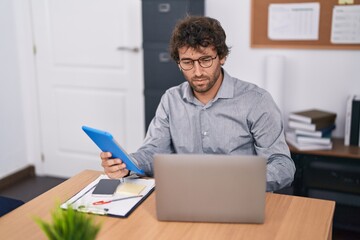Young hispanic man business worker using touchpad and laptop at office