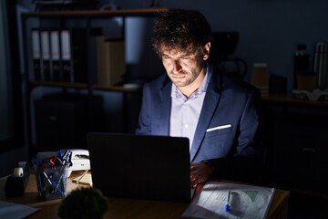 Hispanic young man working at the office at night skeptic and nervous, frowning upset because of problem. negative person.