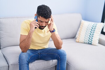 Fototapeta premium Young arab man talking on smartphone with worried expression at home