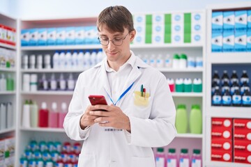 Young caucasian man pharmacist using smartphone working at pharmacy