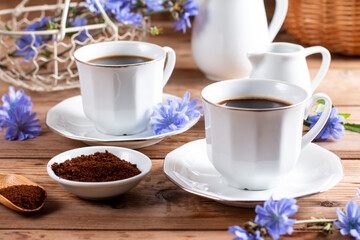 Drink made of chicory roots in cup, blooming chicory plants and spoon with granulated chicory root powder on wooden table. Caffeine free alternative to coffee.