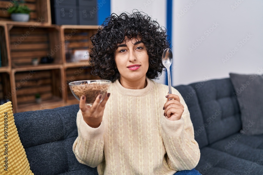 Sticker young brunette woman with curly hair eating healthy whole grain cereals with spoon relaxed with seri