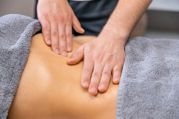 Fototapeta na wymiar Hands massaging a female belly. Therapist applying pressure on the abdomen. Woman getting treatment at spa