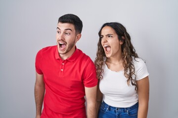 Naklejka premium Young hispanic couple standing over isolated background angry and mad screaming frustrated and furious, shouting with anger. rage and aggressive concept.