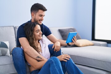 Obraz premium Young hispanic couple using touchpad sitting on sofa at home
