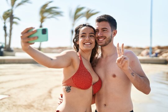 Young hispanic couple tourists wearing swimsuit make selfie by smartphone at seaside