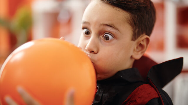 Adorable hispanic boy wearing halloween costume inflating balloon at home