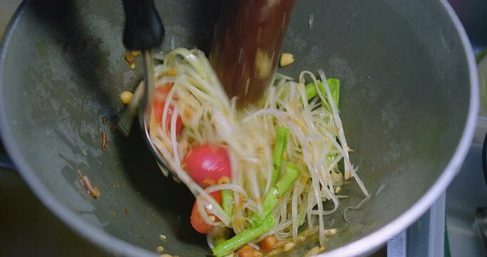 Close up Chef Preparing cooking mixing green papaya salad or Som Tam thai mixed salad with vegetables in a mortar by the pestle and spoon