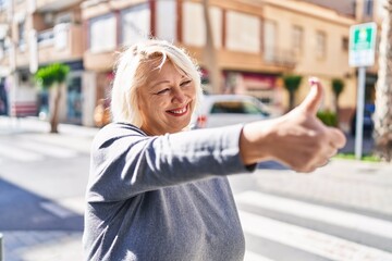 Middle age blonde woman smiling confident doing ok sign with thumb up at street