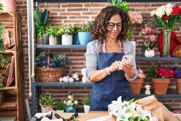 Middle age woman florist smiling confident using smartphone at flower shop