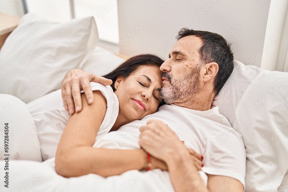 Wall mural middle age man and woman couple hugging each other lying on bed at bedroom