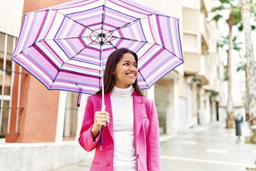 Young latin woman smiling confident holding umbrella standing at street