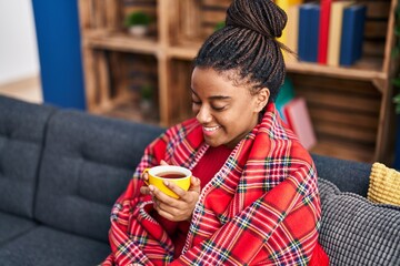 African american woman drinking coffee sitting on sofa at home