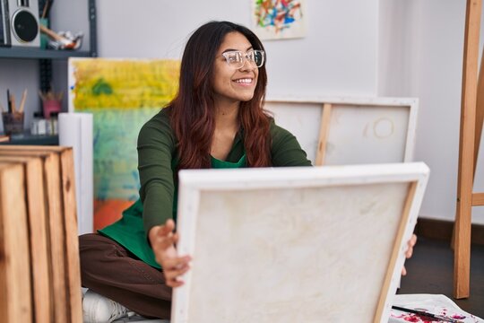 Young hispanic woman artist looking canvas draw at art studio