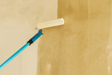 Worker priming walls in new building. Roller brush with prime covering plaster walls. Construction...