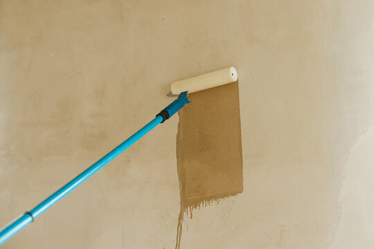 Process of priming walls in new building. Roller brush with prime covering plaster walls. Construction of house and home renovation concept.