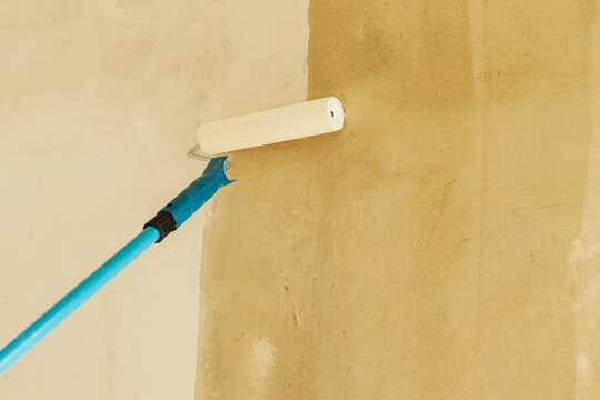 Worker priming walls in new building. Roller brush with prime covering plaster walls. Construction of house and home renovation concept.