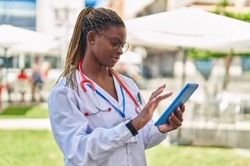 African american woman doctor smiling confident using touchpad at park