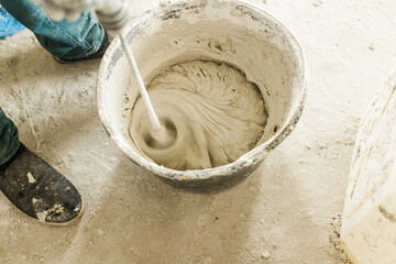 Worker mixing gypsum plaster with water for plastering walls. Construction of house and home renovation concept. Close up of bucket with putty mix and handyman hands