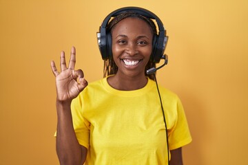 African american woman listening to music using headphones smiling positive doing ok sign with hand and fingers. successful expression.