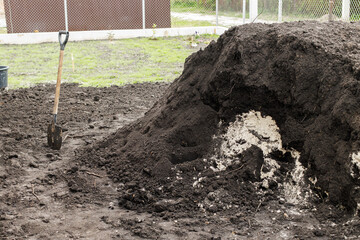 Black soil pile and showel in backyard. Landscaping yard and garden work concept. Clean soil for...